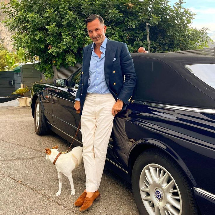 Homme en veste bleu marine et pantalon clair près d’une voiture