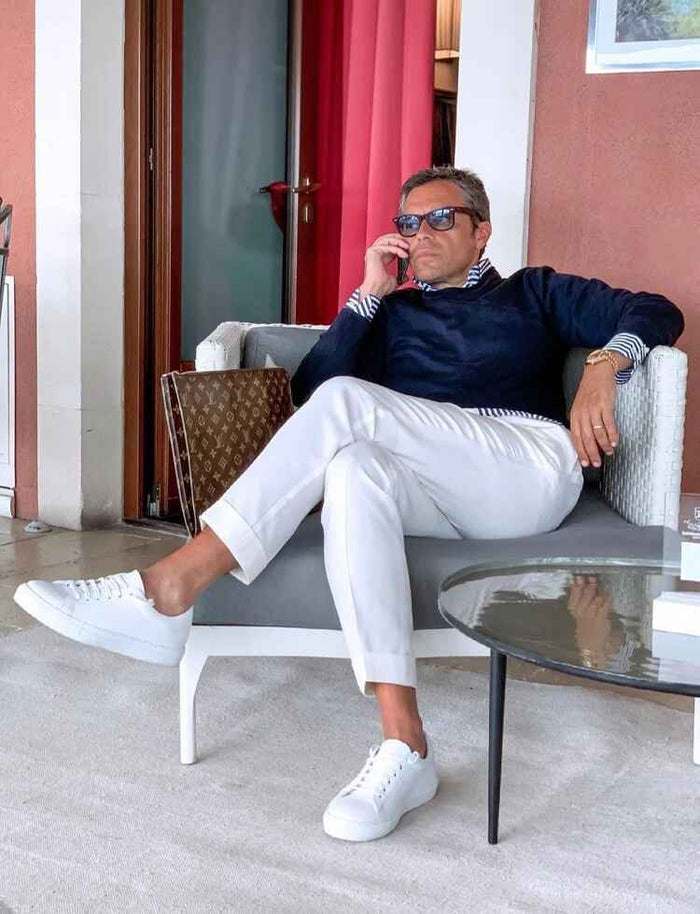 Homme assis en veste bleu marine et pantalon blanc