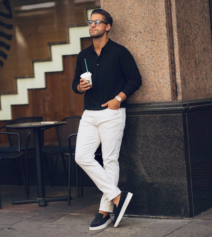 Homme en pull sombre et pantalon blanc près d’un escalier